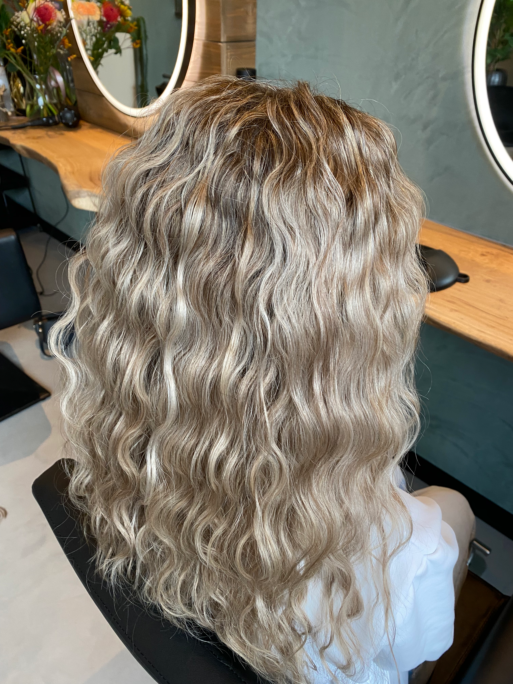 Lange blonde golven van achteren, in de studio met ronde spiegel en eikenhouten werkblad